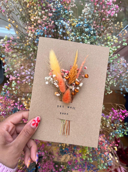 Handmade 'Get Well Soon' card featuring dried flowers arranged in a slot, which can be removed and placed in a small vase. The card is crafted with care, offering a thoughtful and long-lasting gesture of warmth and recovery.