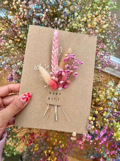 Handmade 'Welcome Baby Girl' card with dried flowers arranged in a removable slot. The flowers can be taken out and placed in a small vase, creating a lasting keepsake to celebrate the arrival of a baby girl.