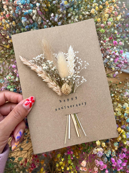 Handmade 'Happy Anniversary' card with dried flowers arranged in a removable slot. The flowers can be taken out and placed in a small vase, creating a lasting keepsake for the special occasion.