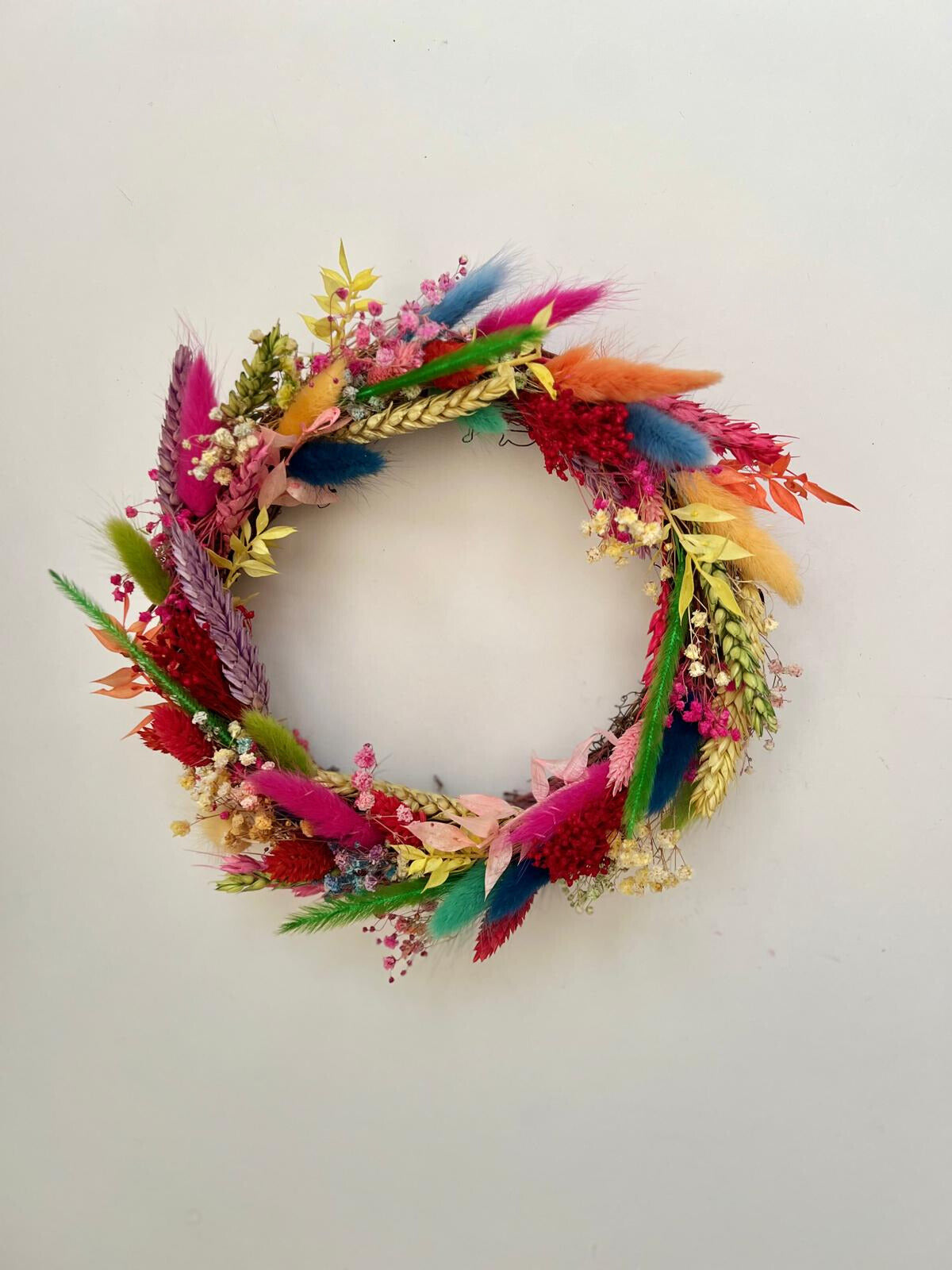 A charming mini Christmas wreath featuring a vibrant mix of colourful dried flowers and seasonal accents, perfect for holiday décor